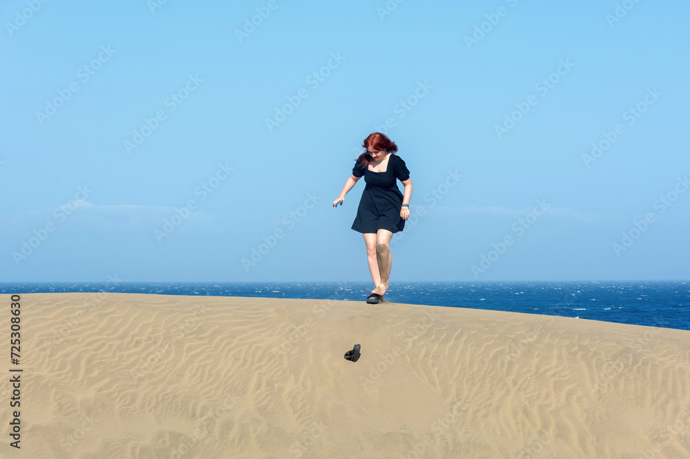Young girlin a black summer dress stands on a sand dune and has lost a shoe Young girlin a black summer dress stands on a sand dune and has lost a shoe