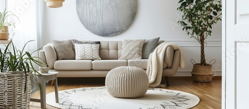 Place a pouf next to a beige couch with cushions in a living room featuring a white circular rug and a silver artwork.