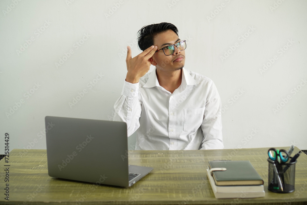 young asian businessman in a workplace with problems making suicide gesture, wearing white shirt with glasses isolated young asian businessman in a workplace with problems making suicide gesture, wearing white shirt with glasses isolated