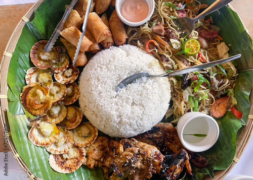 Filipino food on a plate with a banana leaf base. Rice, chicken, lumpia, pansit photo