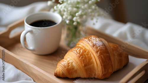 Delicious croissant with a cup of coffee on a tray in bed