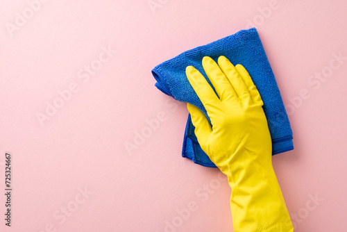 A first-person perspective photo featuring a hand in a rubber glove, using a soft cleaning cloth on a gentle pink background, perfect for housecleaning ads with space for text