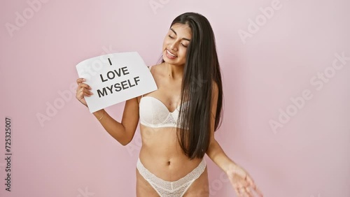 Young, confident indian woman with long hair and a gleaming smile, pointing her finger up, holding 'love my body' text over pink isolated background - a beautiful expression of body positivity. photo