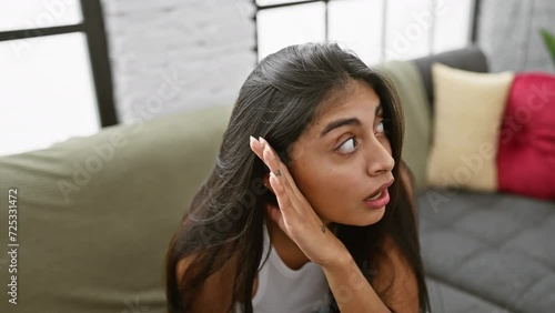 Deafness no barrier! young indian woman homebound, relaxes on sofa, listening to rumors and gossip with hand on ear
