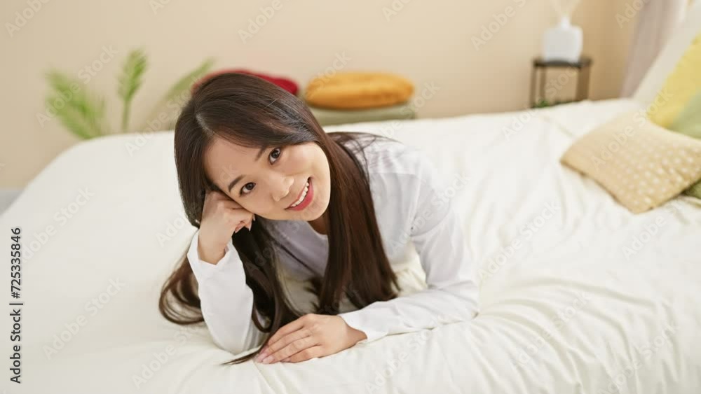 A smiling asian woman lying on a bed in a bright bedroom, exuding a relaxed and cozy atmosphere A smiling asian woman lying on a bed in a bright bedroom, exuding a relaxed and cozy atmosphere