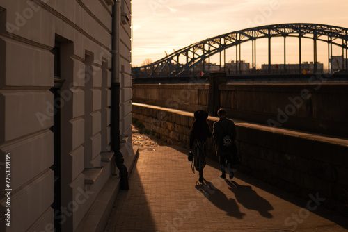 Two people walking across the river with the bridge on background © Oleksandr