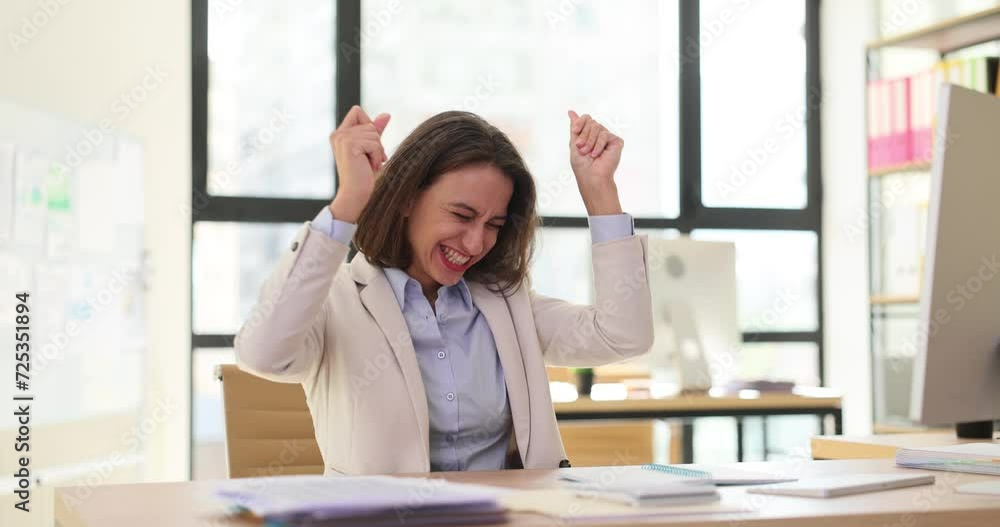 Adult business woman manager dances sitting at office desk and successful computer win Adult business woman manager dances sitting at office desk and successful computer win