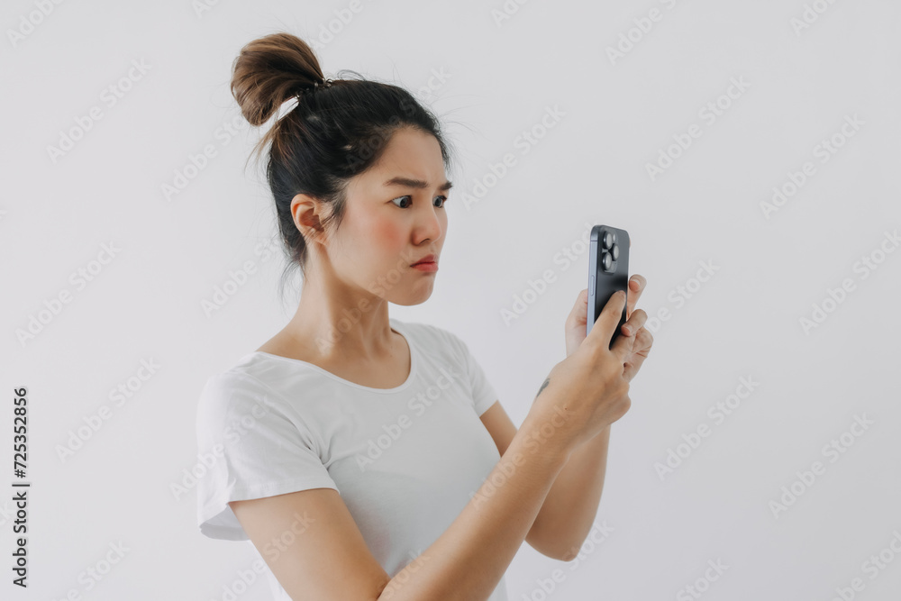 Asian Thai woman using mobile phone with funny doubt face, holding smartphone by silent suspicious, standing isolated over white background wall. Asian Thai woman using mobile phone with funny doubt face, holding smartphone by silent suspicious, standing isolated over white background wall.