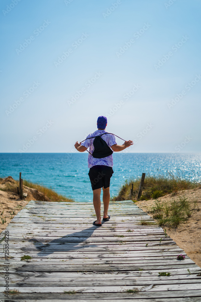 Man walking towards the beach on a wooden path in summer.