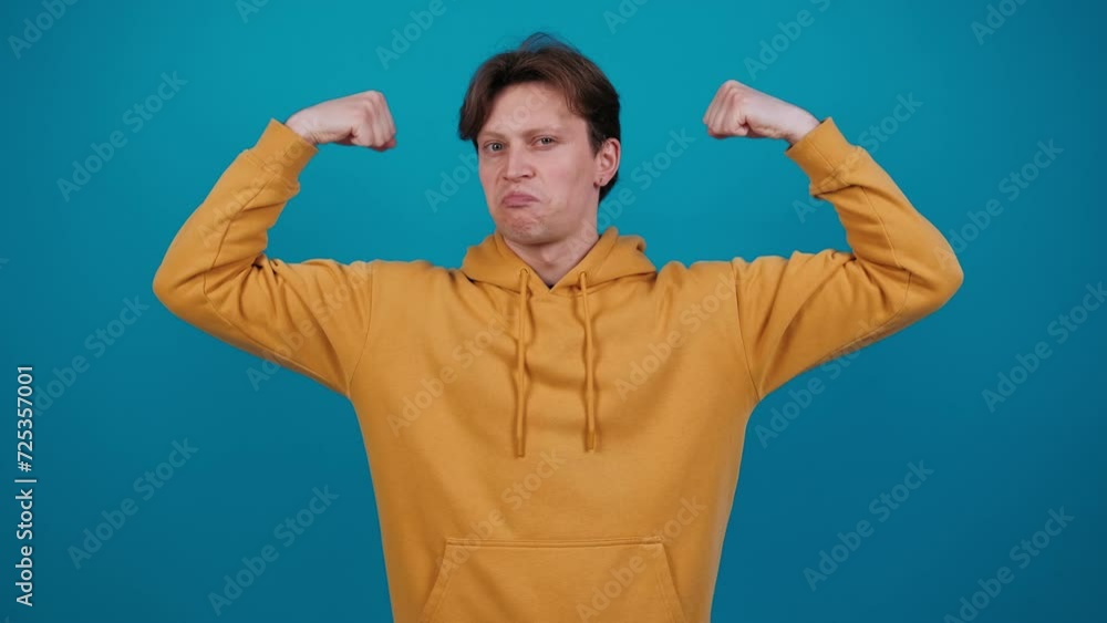 Happy smiling guy showing bicep with confident expression, bodybuilding strength power. Arm, bicep, muscle and athletic man for fun, sport, health and fitness. Studio shot isolated on blue background