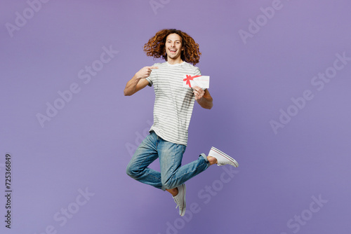 Full body young smiling man he wears grey striped t-shirt casual clothes hold gift certificate coupon voucher card for store isolated on plain pastel light purple background studio. Lifestyle concept.