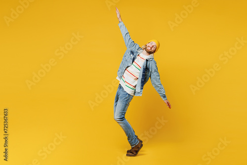 Full body side view young man he wearing denim shirt hoody beanie hat casual clothes stand on toes with outstretched hands arms isolated on plain yellow background studio portrait. Lifestyle concept.