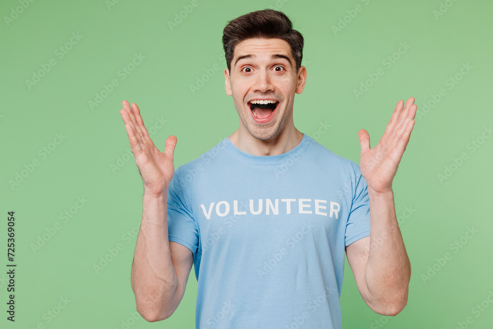 Young surprised shocked man wears blue t-shirt white title volunteer look camera spread hands isolated on plain pastel light green background Voluntary free work assistance help charity grace concept Young surprised shocked man wears blue t-shirt white title volunteer look camera spread hands isolated on plain pastel light green background Voluntary free work assistance help charity grace concept