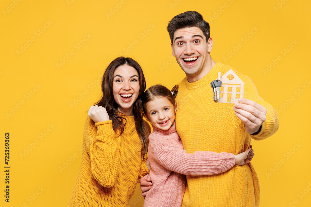Young happy fun parents mom dad with child kid girl 7-8 years old wearing pink sweater casual clothes hold keys, house mockup do winner gesture isolated on plain yellow background. Family day concept.