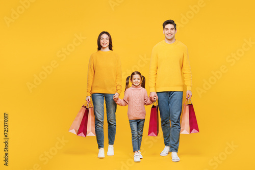 Full body young happy parent mom dad with child kid girl 7-8 years old wear pink sweater casual clothes hold shopping package bag isolated on plain yellow background Black Friday sale buy day concept.