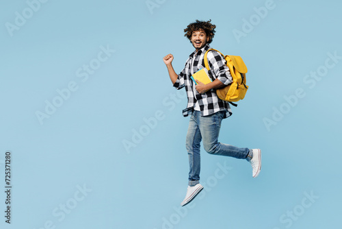 Full body young Indian boy student wear shirt casual clothes backpack bag hold books jump high do winner gesture isolated on plain pastel light blue background. High school university college concept.