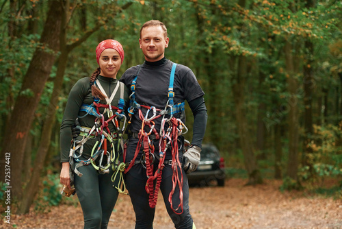 Standing and posing. Man and woman doing climbing in forest with use of safety equipment