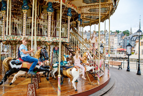 Canvas Print Adorable little girl and school kid boy having a ride on the old vintage merry-go-round in city of Honfleur France