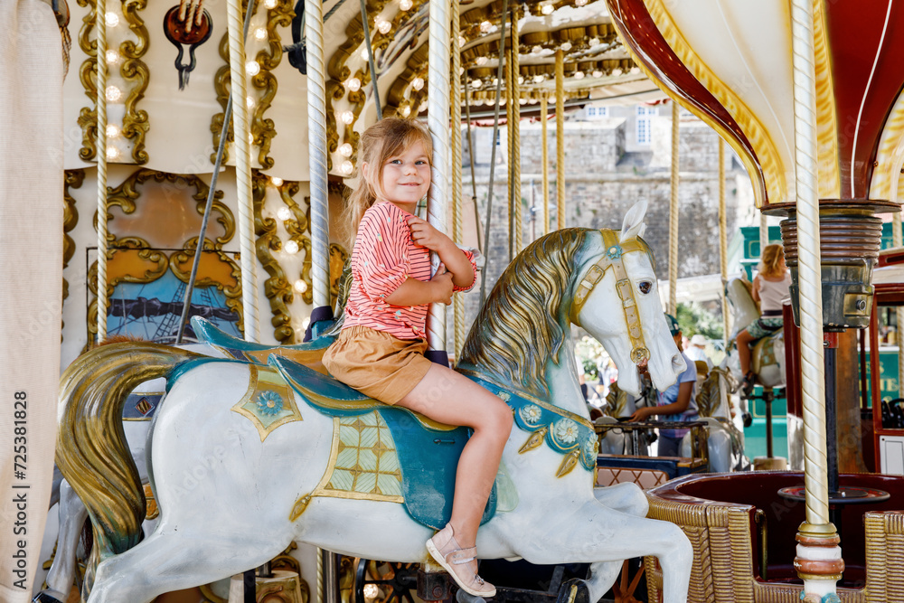 Happy positive preschool girl having a ride on the old vintage merry-go-round in city of St Malo France. Smiling child on a horse.