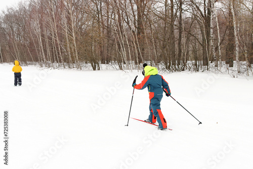 Boys in overalls goes skiing along the edge of the forest