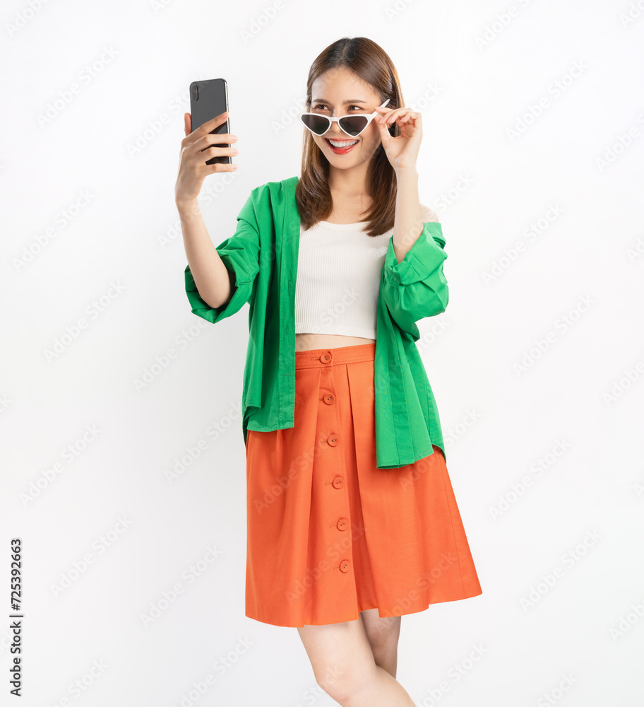 Cheerful beautiful Asian women wear colorful clothes and holding smartphone with looking on screen, white background. Cheerful beautiful Asian women wear colorful clothes and holding smartphone with looking on screen, white background.