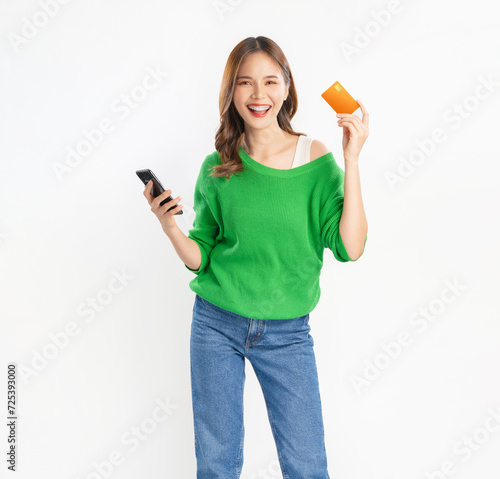 Cheerful young asian woman in green shirt with holding credit card and using smartphone on isolated white background.