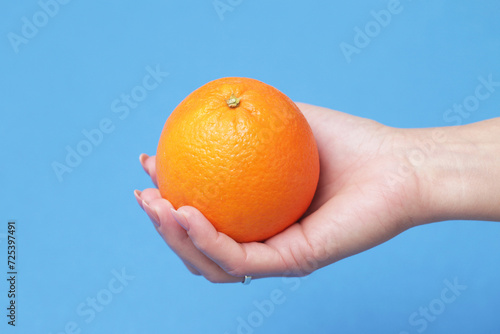 Hand holding an orange. Orange isolated on blue screen. Woman holding fruit with her hand. Cutout body part.