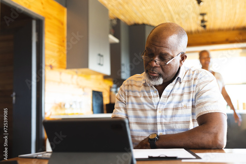 Senior african american man doing paperwork using tablet at home photo