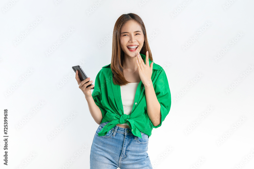 Cheerful beautiful Asian woman wearing green shirt and holding smartphone with smile and hand touching mouth on white background. Cheerful beautiful Asian woman wearing green shirt and holding smartphone with smile and hand touching mouth on white background.