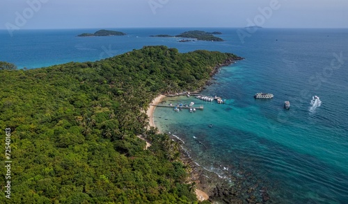 Aerial view of a tropical island with lush greenery, a sandy beach, and boats on clear blue waters, ideal for vacation and travel concepts, Earth Day concept