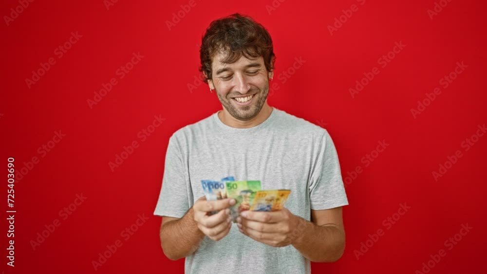 Young man counting swiss francs banknotes smiling over isolated red background Young man counting swiss francs banknotes smiling over isolated red background