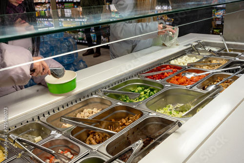 Fresh Salad bar counter with person's hands lifting vegetable into a salad bowl. photo