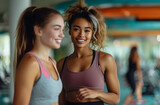 Two young women smiling and chatting in a gym setting.