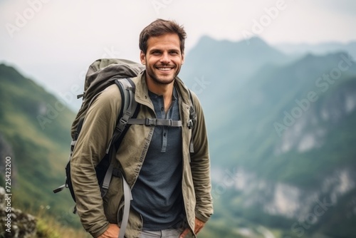 Portrait of a handsome young man with backpack standing on top of a mountain
