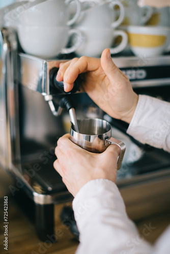 A barista prepares milk for cappuccino using an espresso machine. Close-up of a man preparing coffee in a cafe.