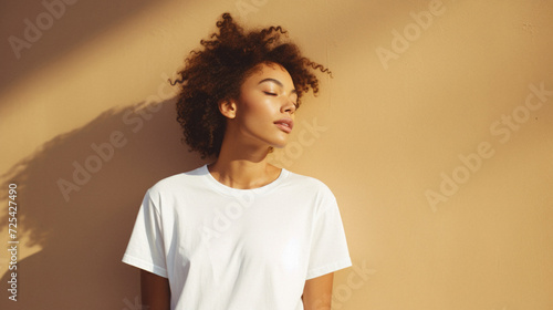 Young adult pretty African American woman model wearing white t-shirt with eyes closed on background. Face flawless fresh skin hair care cosmetic treatment makeup products skincare ad. Beauty portrait