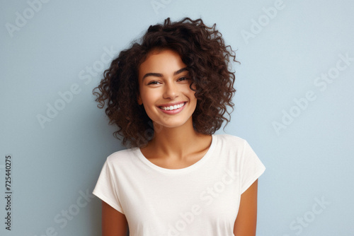 Young happy smiling Latin woman model wearing tshirt standing on color background. Face skin treatment, curly hair care cosmetics makeup, fashion ads. Beauty portrait. White t-shirt mock up template . © Synthetica