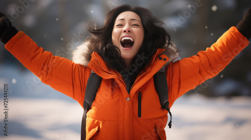 Woman wearing orange jacket raises her hands in air. This image can be used to depict excitement, celebration, or freedom