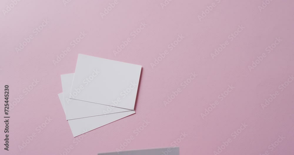Hand holding piece of paper over pieces of paper with copy space on pink background in slow motion Hand holding piece of paper over pieces of paper with copy space on pink background in slow motion