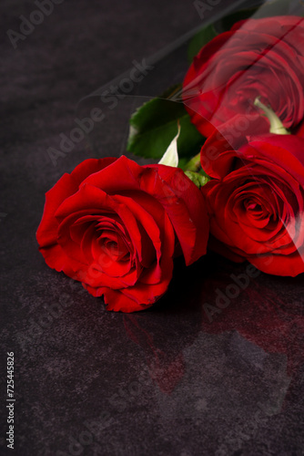 Set of three red roses in a bouquet laying on a dark grey textured surface. Vertical image with copy space.