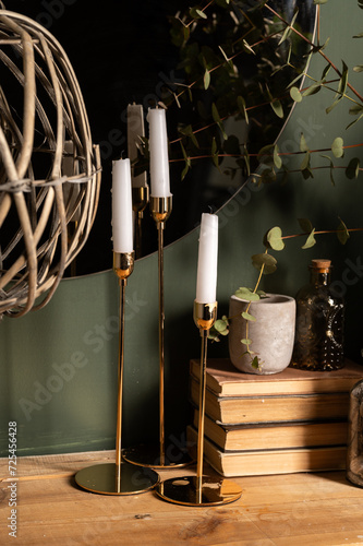 green eucalyptus branches in a vase with books and candles on a wooden table