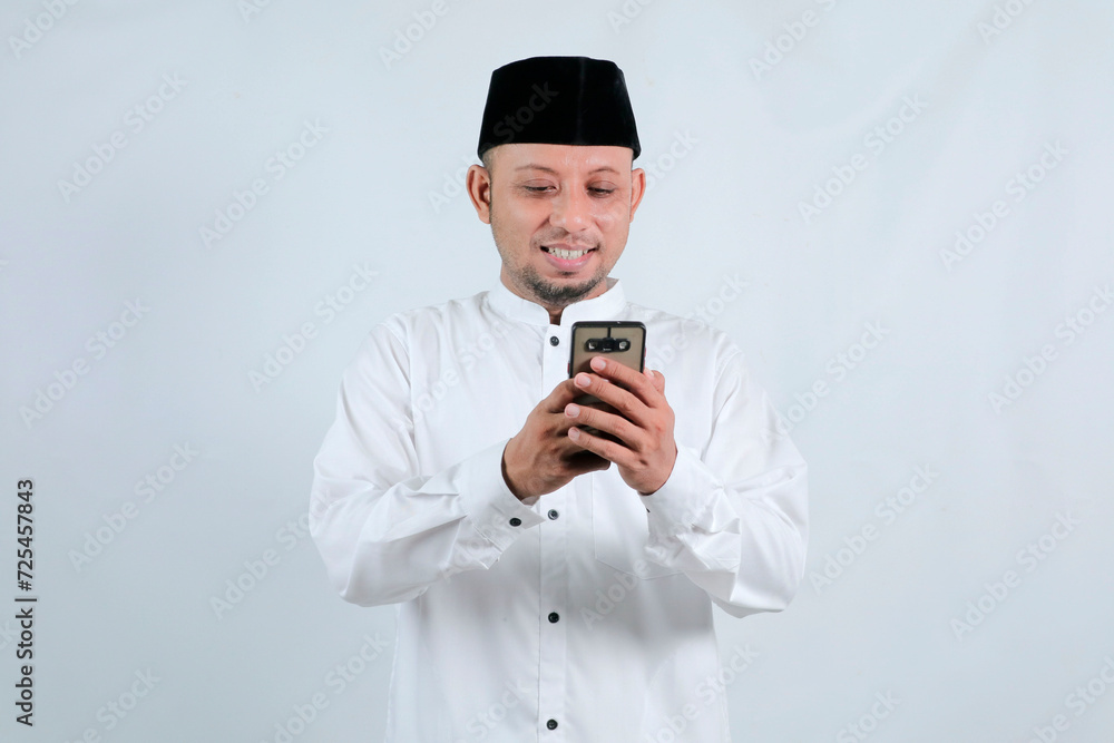 Happy asian muslim man holding and pointing on phone cellular over white background. Ramadan concept Happy asian muslim man holding and pointing on phone cellular over white background. Ramadan concept