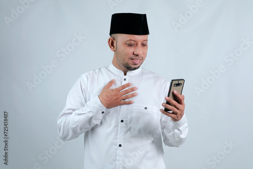 Happy asian muslim man holding and pointing on phone cellular over white background. Ramadan concept