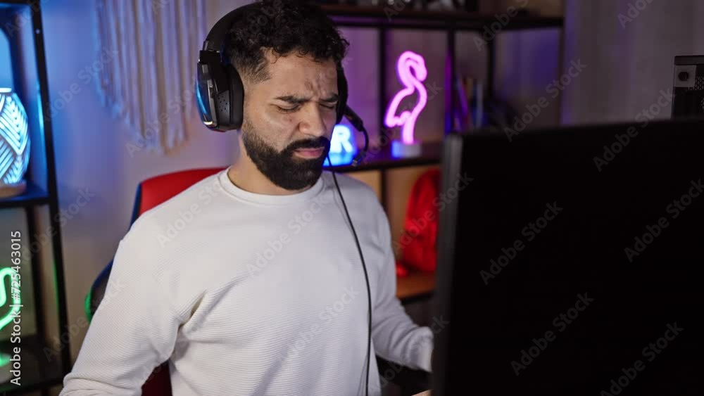 A bearded man expressing discomfort while gaming at night in a dark room with neon lights and a headset. A bearded man expressing discomfort while gaming at night in a dark room with neon lights and a headset.