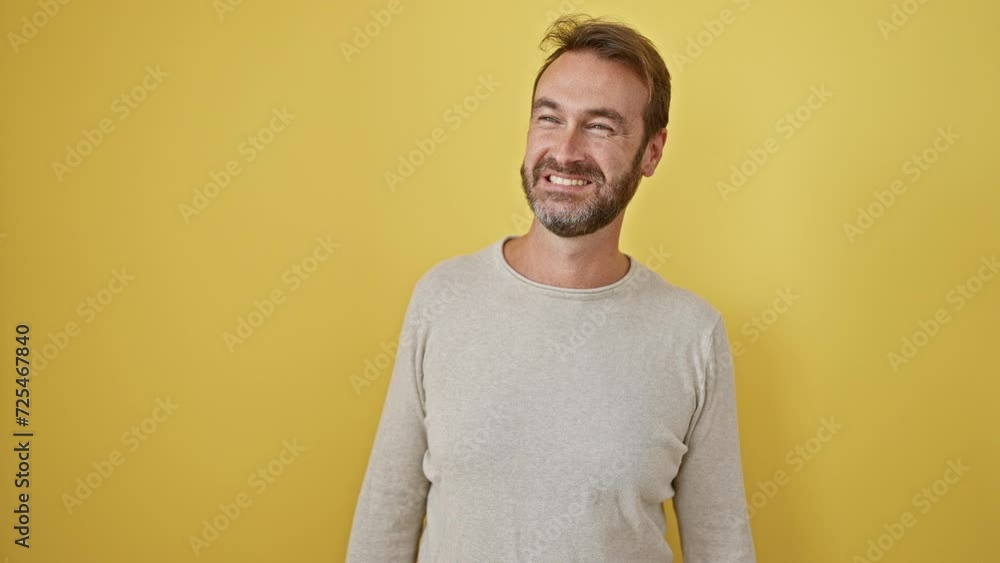 Young hispanic man standing looking away to side with smile on face, natural expression. laughing confident. over isolated yellow background Young hispanic man standing looking away to side with smile on face, natural expression. laughing confident. over isolated yellow background