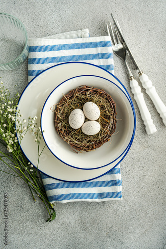 Overhead view of an Easter place setting with  white gypsophila flowers and a bird's nest with painted Easter eggs and feathers photo