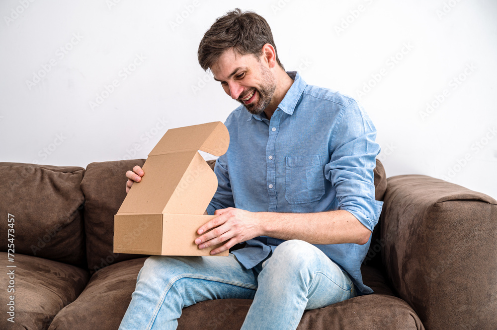 Satisfied young man holding package, opening and looking into box Satisfied young man holding package, opening and looking into box