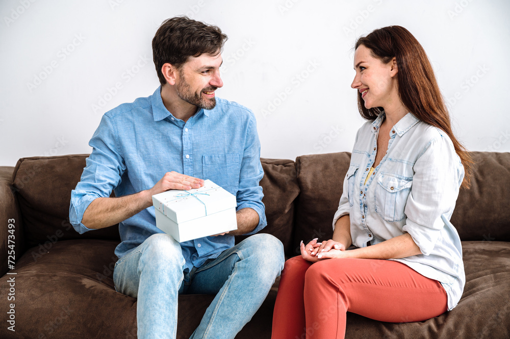 Glad man receive box with gift and open it while sitting on couch with wife Glad man receive box with gift and open it while sitting on couch with wife