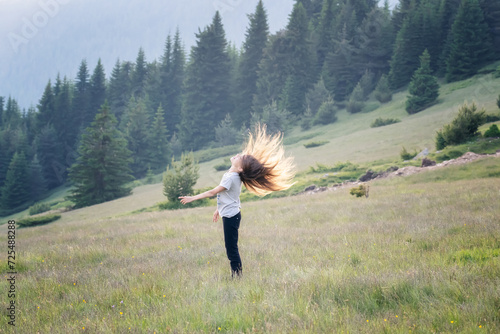 Happy little girl waving long hair and enjoying the spring meadow surrounded by picturesque mountain slopes