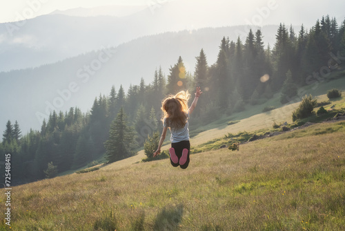 Happy little girl jumping and enjoying life at a spring meadow on the background of a picturesque mountain slopes.